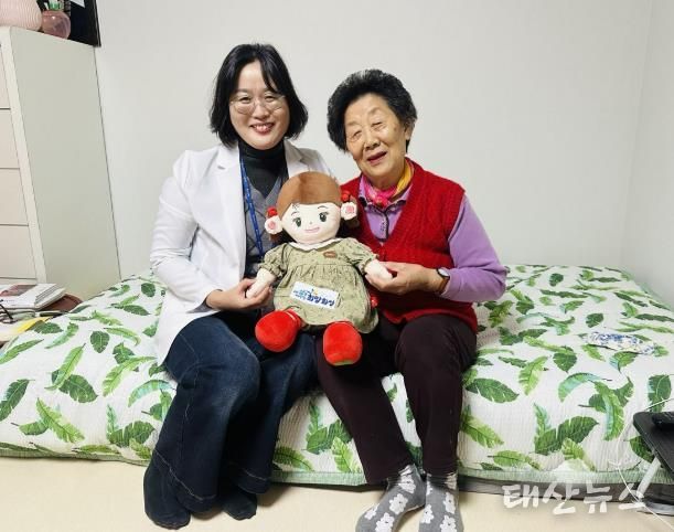 화성시동탄보건소 관계자와 독거 어르신이 AI 돌봄로봇 ‘효돌이’를 함께 들고 환하게 웃고 있다